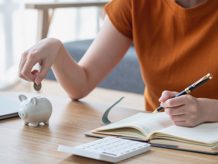 Bild mit einer Frau, die übern Finanzen sitzt und eine Münze in ein Sparschwein tut.