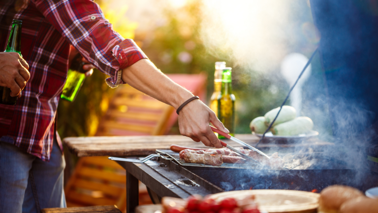 Im Sommer ist jemand am grillen. Würstchen und Gemüse liegen auf dem Grill